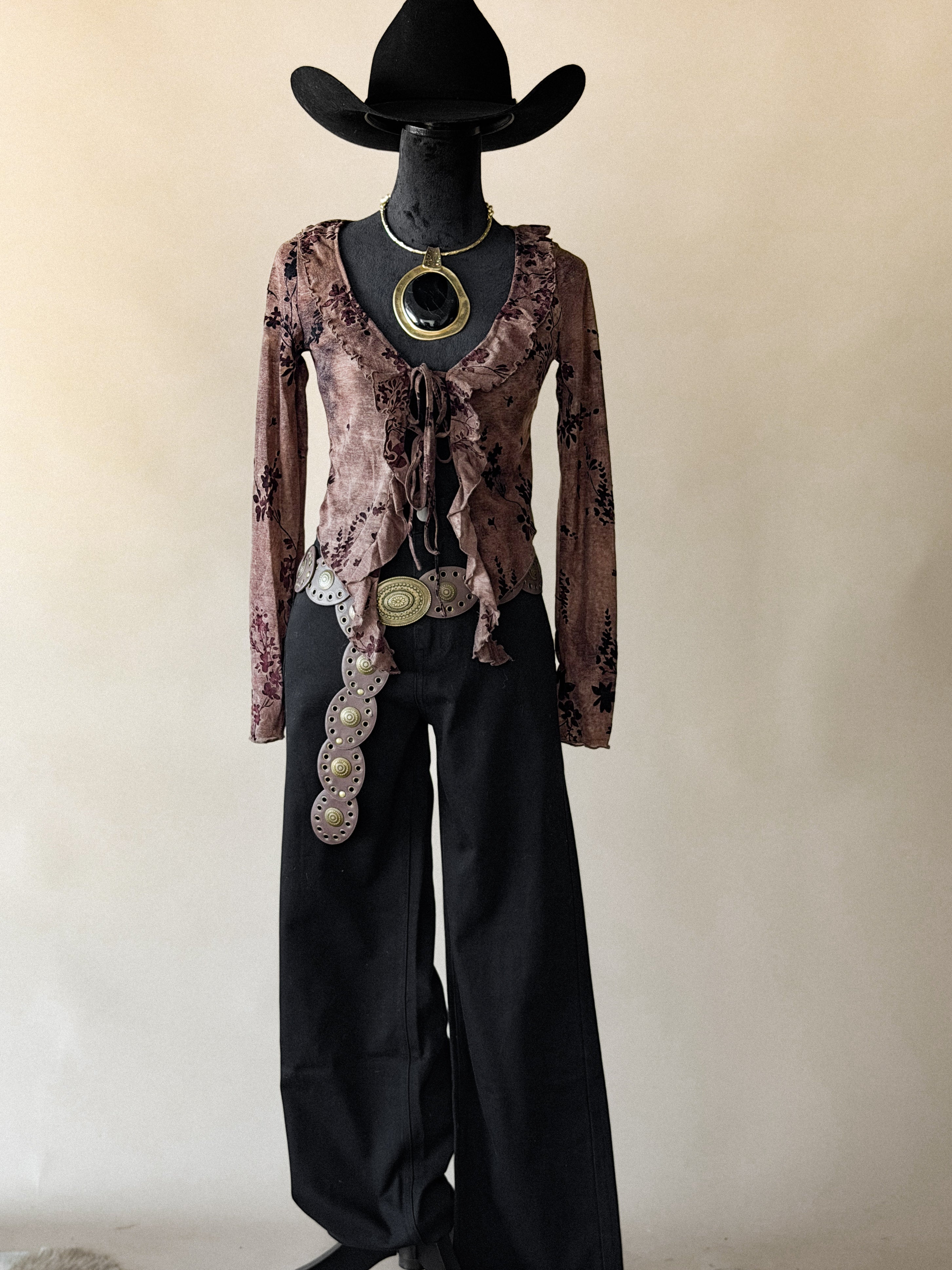 Mannequin wearing a floral top, black pants, and a cowboy hat with a beige background