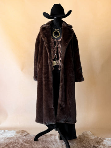 Mannequin wearing a long brown fur coat and black cowboy hat on a beige background