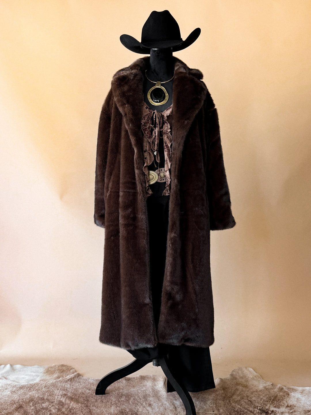 Mannequin wearing a long brown fur coat and black cowboy hat on a beige background
