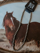 Western silver bead necklace with black tag displayed on horse photo background