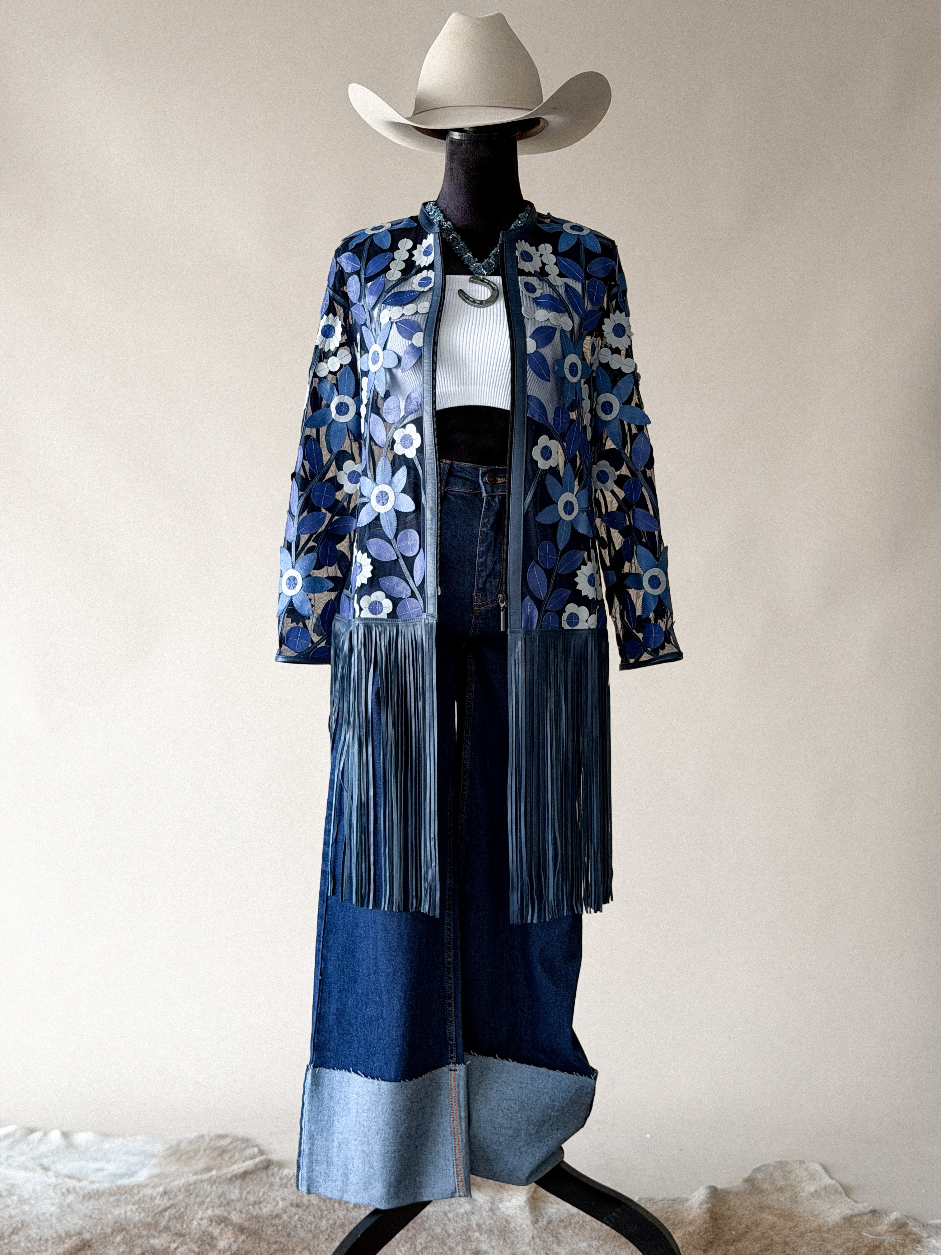 Western boho outfit with floral fringe jacket, wide-leg denim pants, white crop top, and cowboy hat