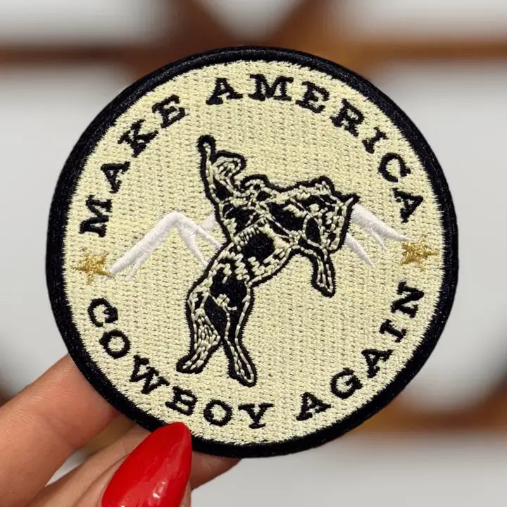 round cream and black embroidered make america cowboy again iron-on patch held in hand