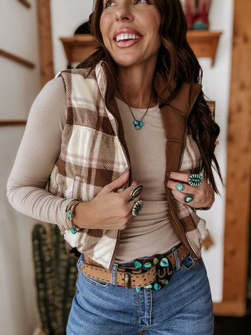 Woman wearing a plaid vest, beige top, and blue jeans with a decorative belt.