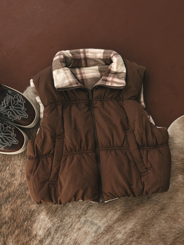 Brown puffer vest with plaid lining on a brown surface