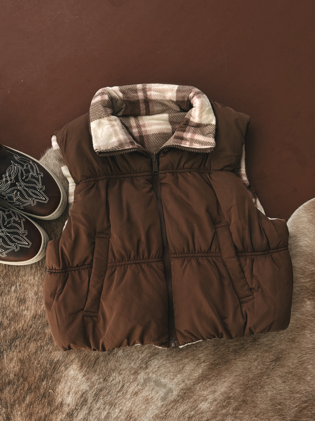 Brown puffer vest with plaid lining on a brown surface