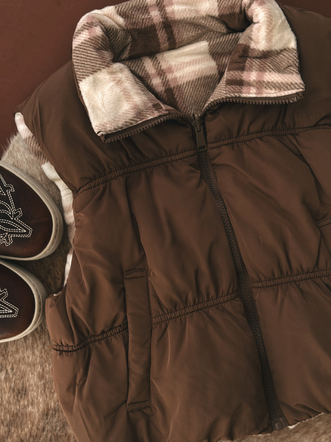 Brown winter coat with plaid lining and matching boots on a brown background