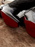 Black western wide calf boots with red soles on brown fur rug, close-up view