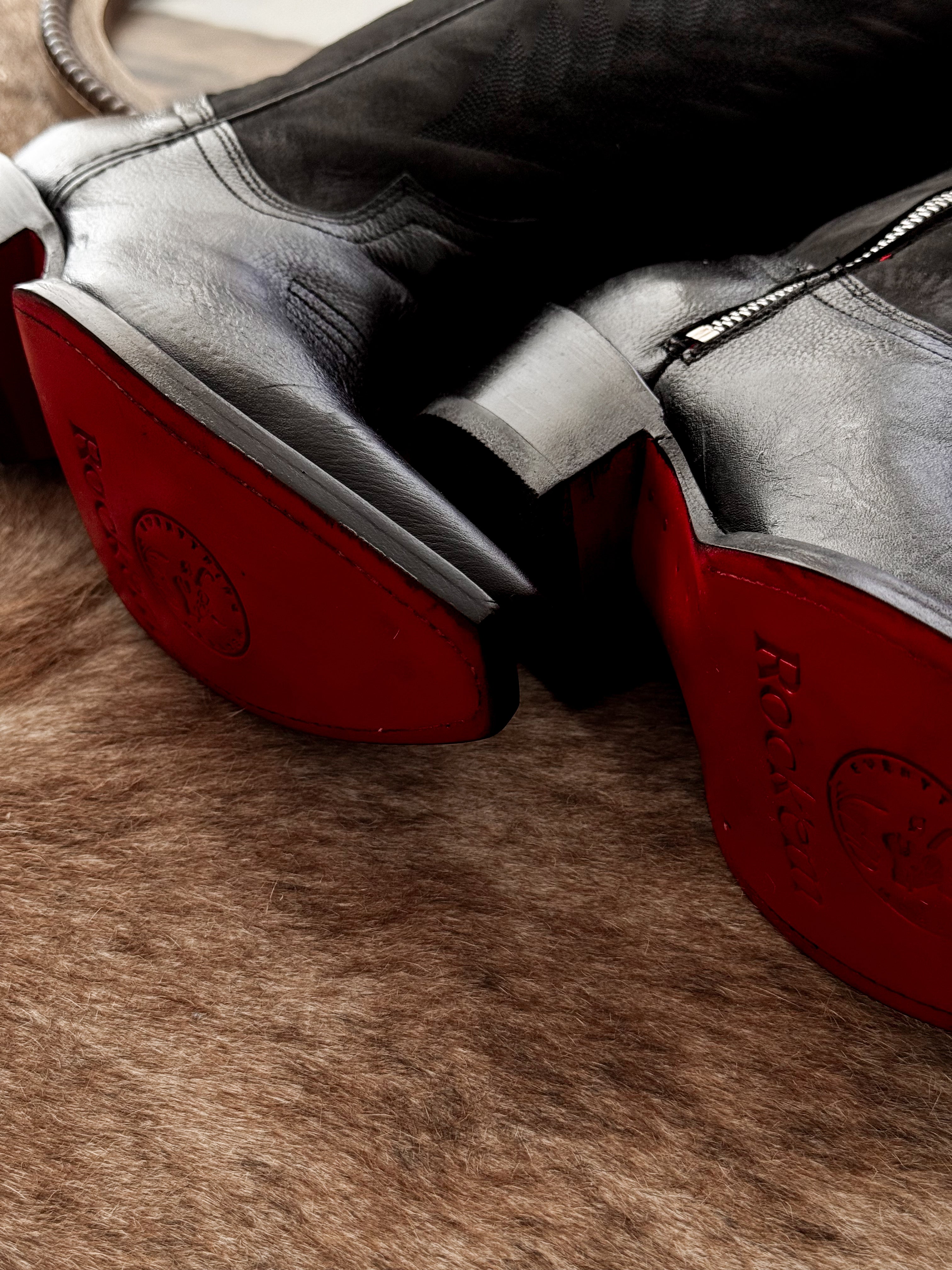 Black western wide calf boots with red soles on brown fur rug, close-up view
