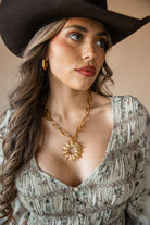 Woman wearing a cowboy hat, floral dress, and gold necklace with a star pendant.