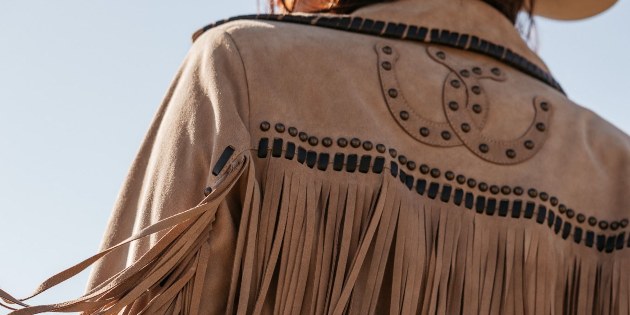 Close-up of a tan leather jacket with fringe and studded details against a clear blue sky.