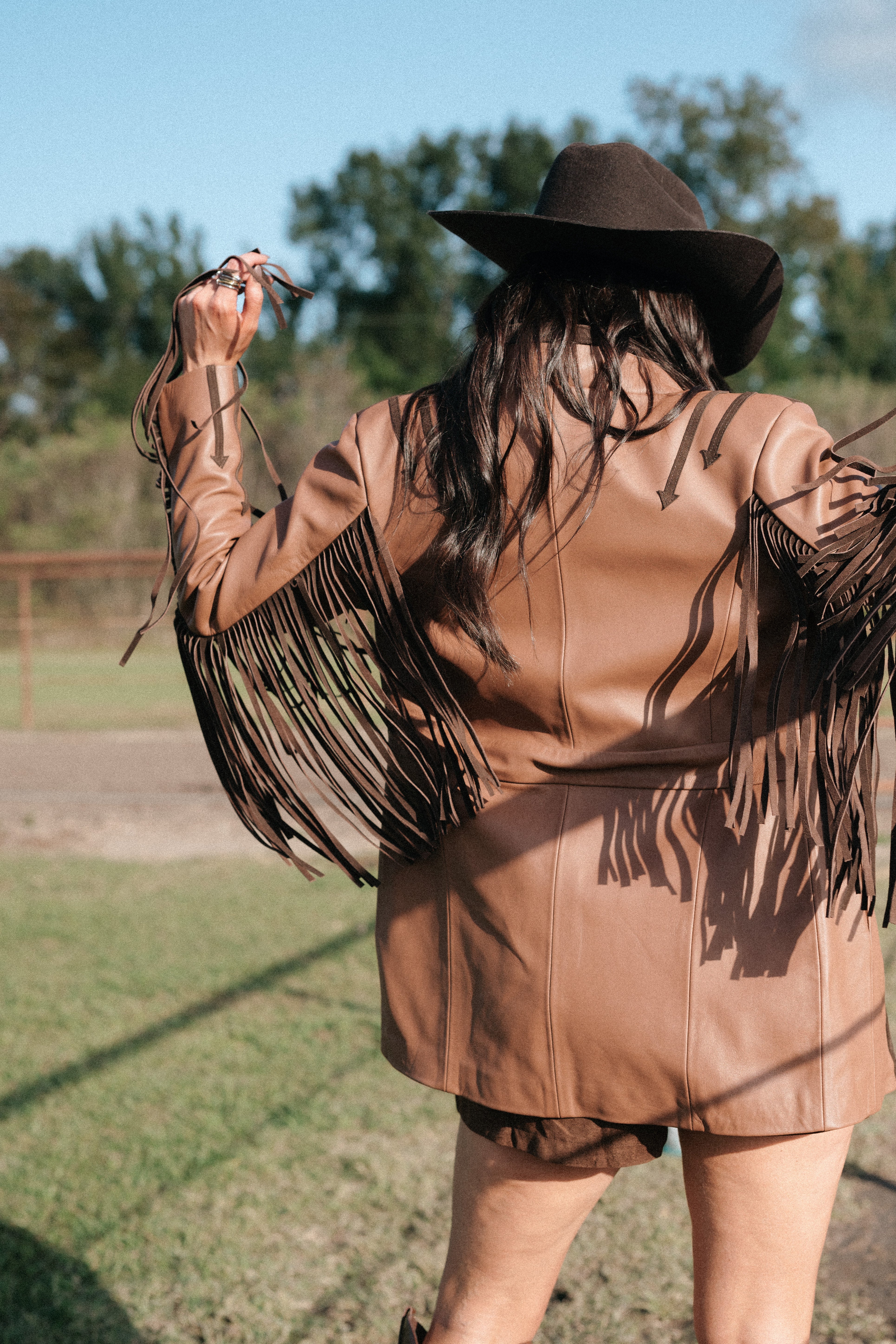 Woman in brown fringe western jacket and cowboy hat outdoors