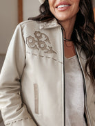Woman wearing a cream western boho jacket with embroidered floral detail and a white top