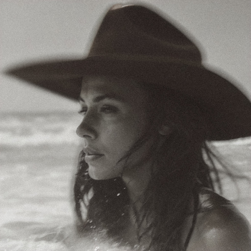 Black and white photo of a person wearing a wide-brimmed hat with water in the background