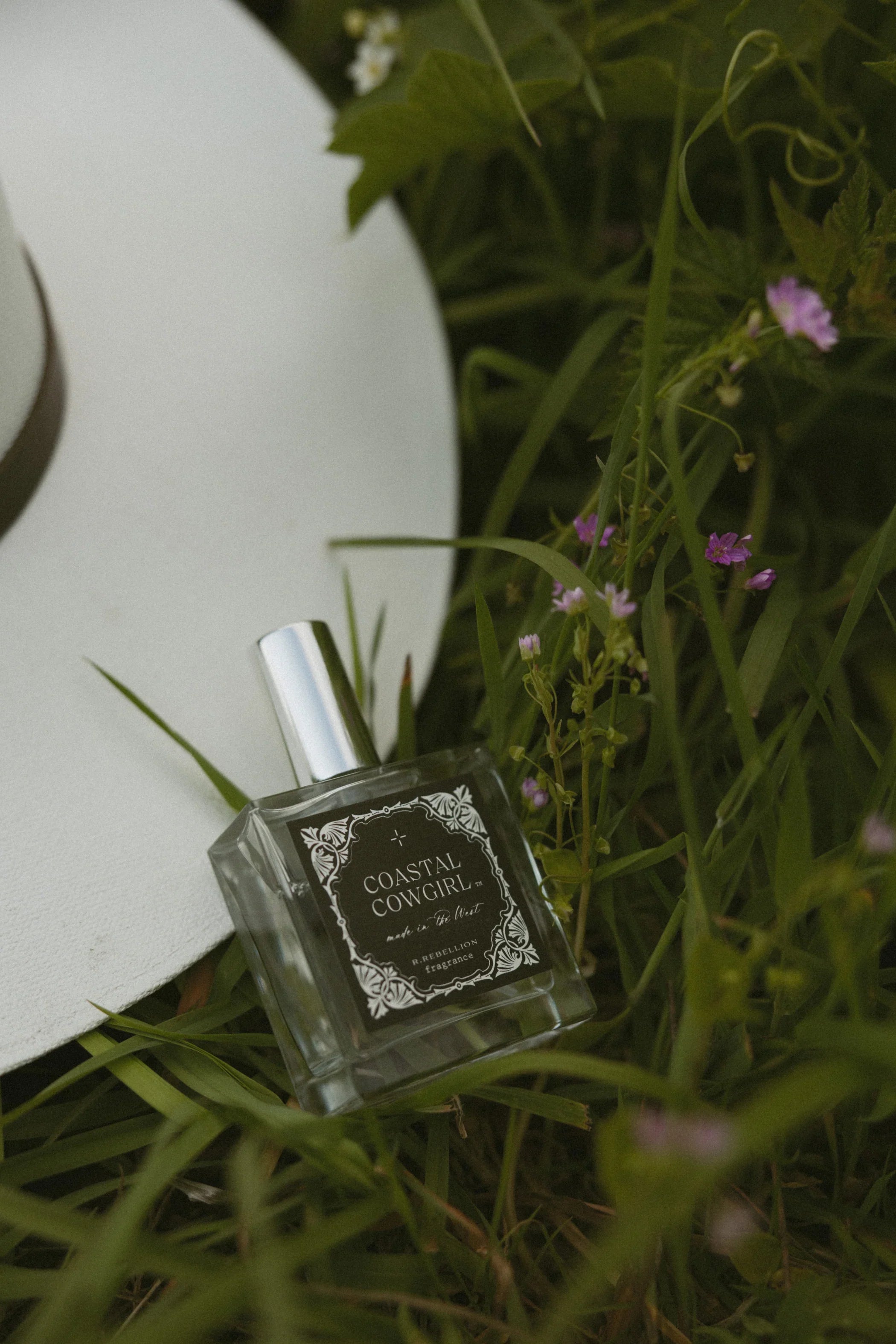 Perfume bottle labeled 'Coastal Cowgirl' on grass with flowers
