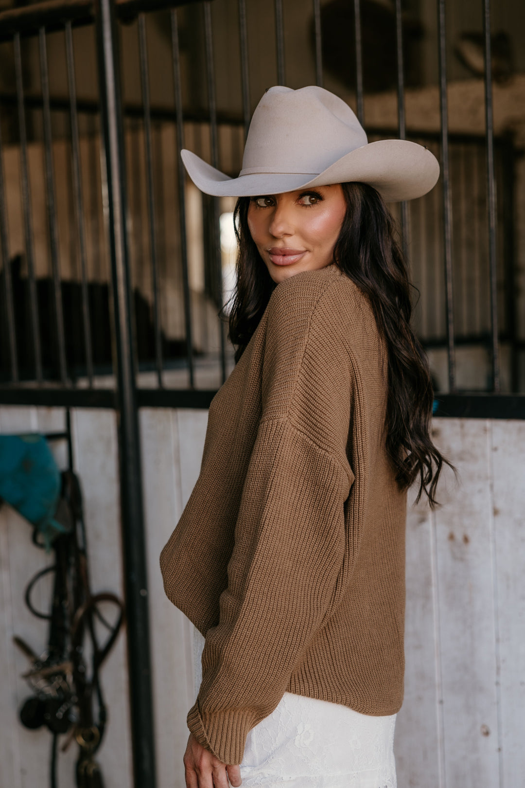 Woman wearing a beige cowboy hat and brown sweater in a rustic setting