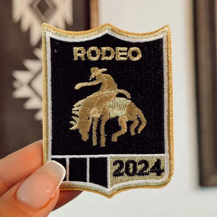 embroidered black and gold rodeo 2024 shield iron-on patch held in hand