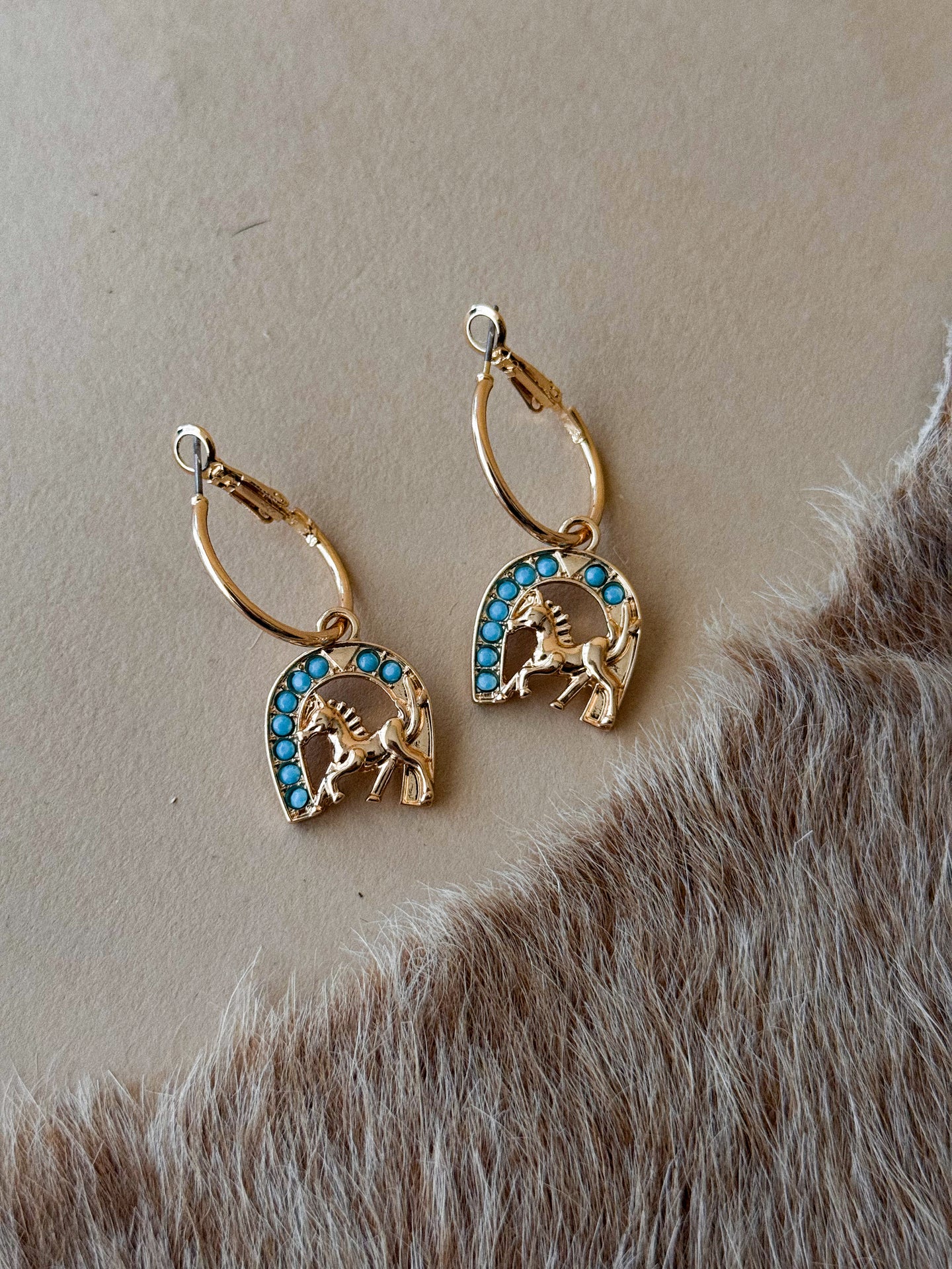 Gold horseshoe earrings with turquoise-style stone accents on neutral background