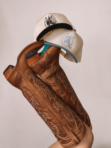 brown cowgirl hat and blue western trucker hat on cowboy boots
