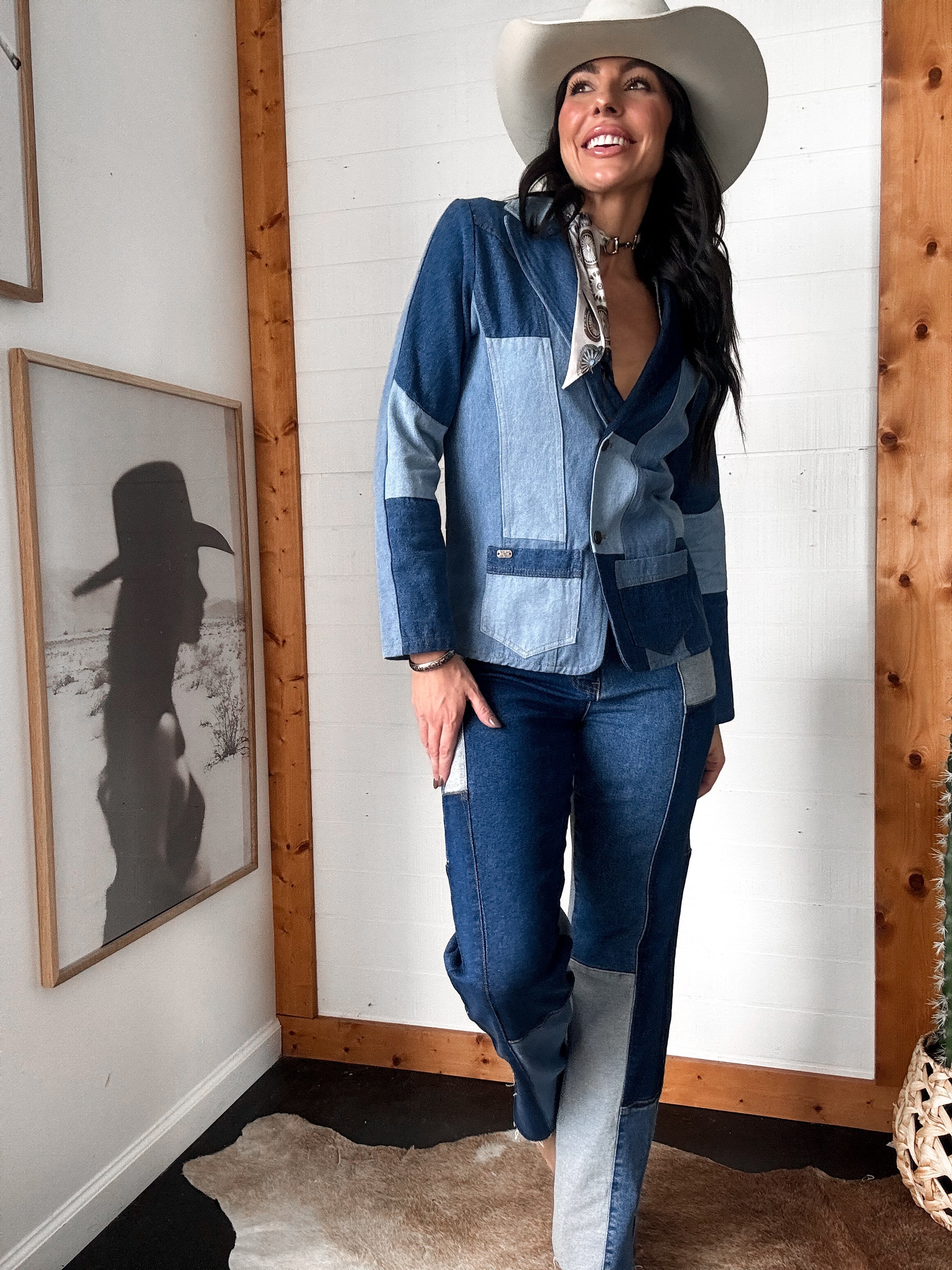 Woman wearing a patchwork denim outfit with a cowboy hat in a room with wooden walls and framed pictures.