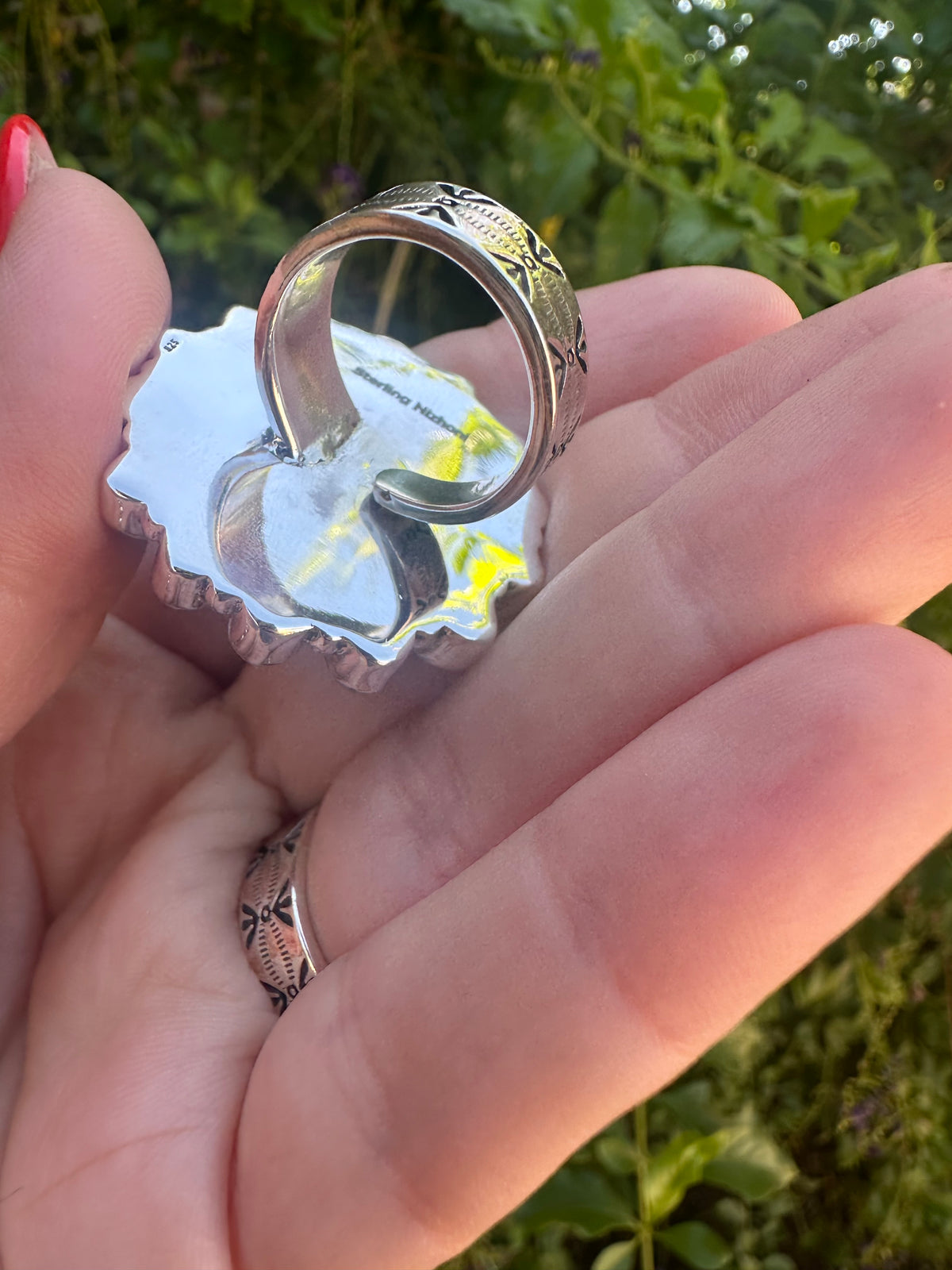 Hand holding a sterling silver horse ring with western engraved details outdoors
