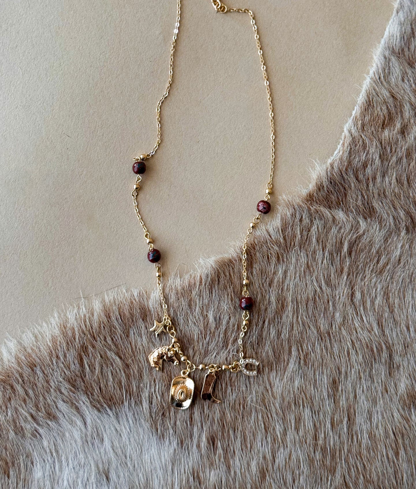 Gold western charm necklace with stone bead accents on faux fur background